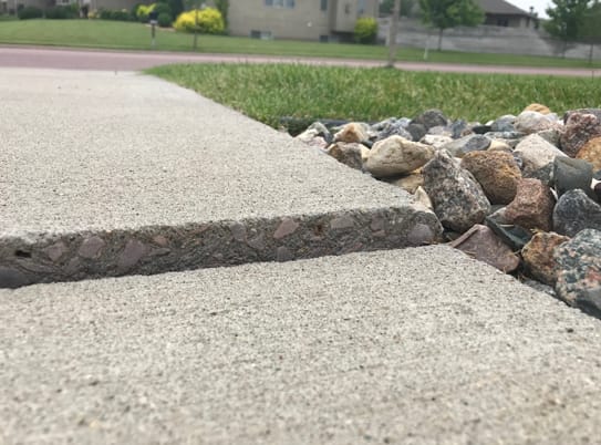 Sunken concrete sidewalk creating a tripping hazard near a home